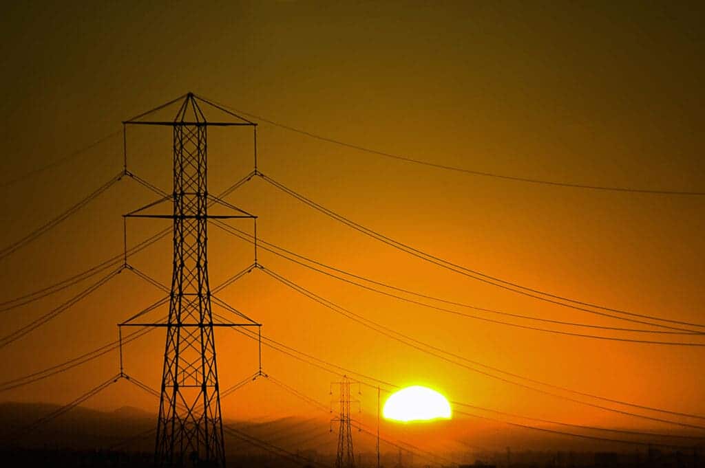 The sun is setting over a field of electricity pylons.