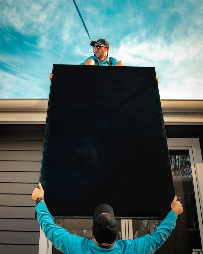 A man holding a solar panel on top of a house.