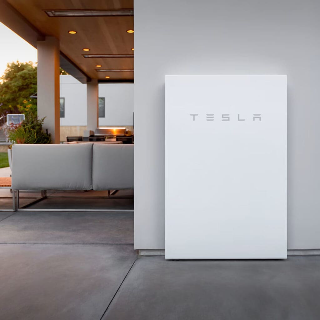 Tesla Powerwall battery. A large white battery stands against the outer wall of a modern home.