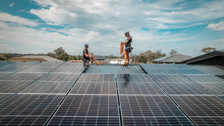 Two people working on solar panels on a roof.