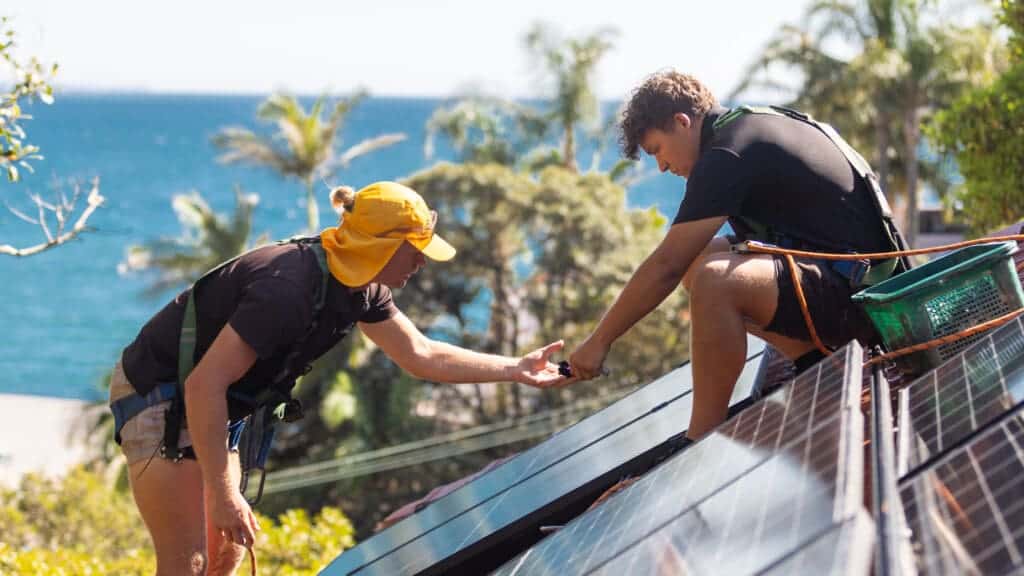 Two men working on solar panels on a roof.