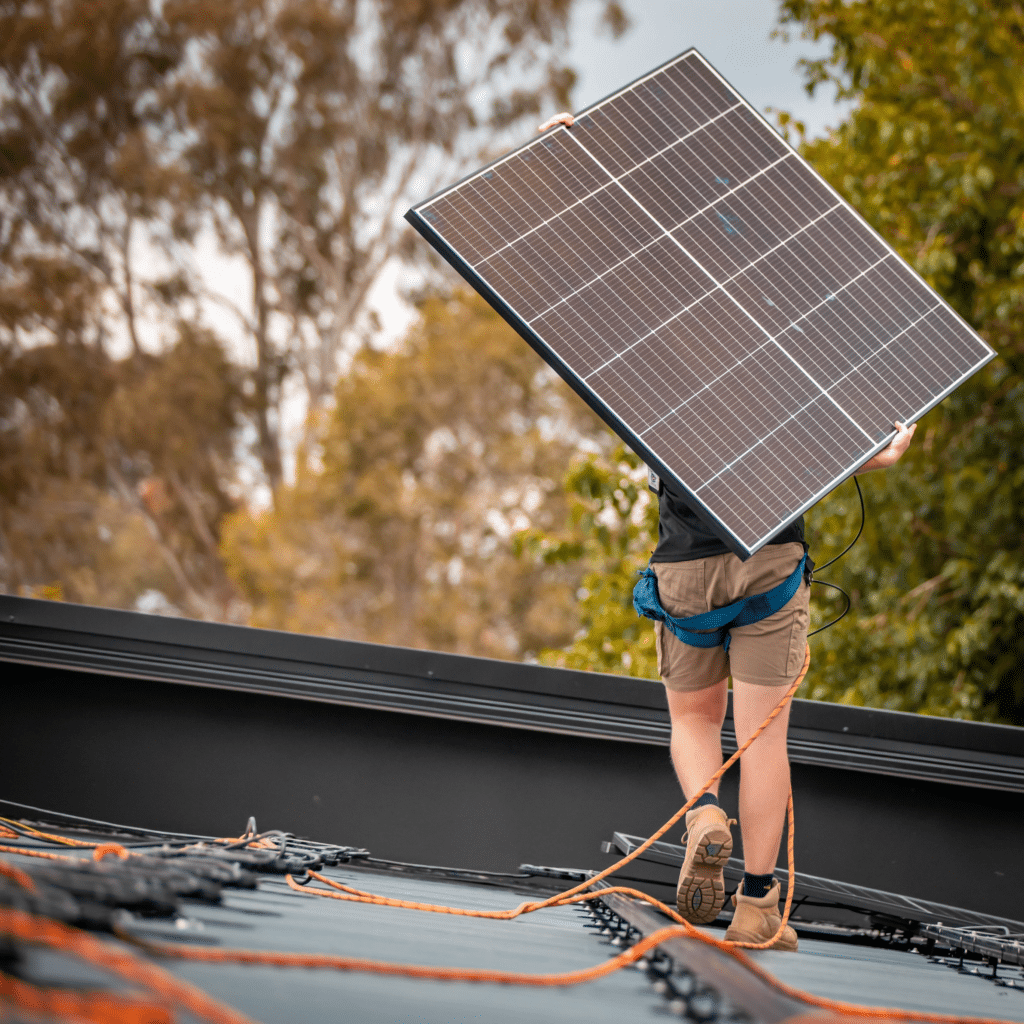 A man carrying a solar panel on top of a roof.