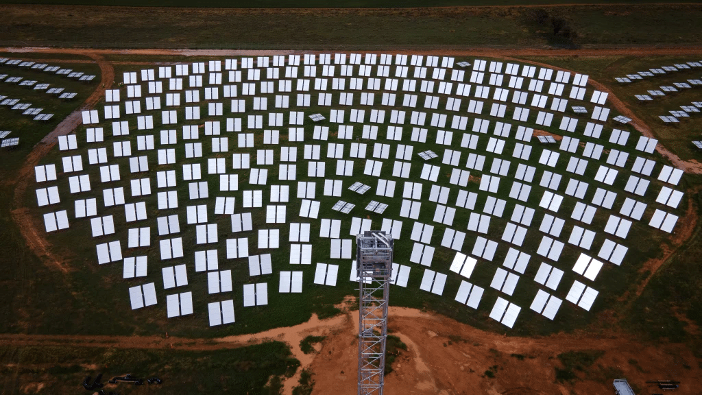 Aerial view of a solar power plant with rows of photovoltaic panels arranged in a circular pattern around a central tower.