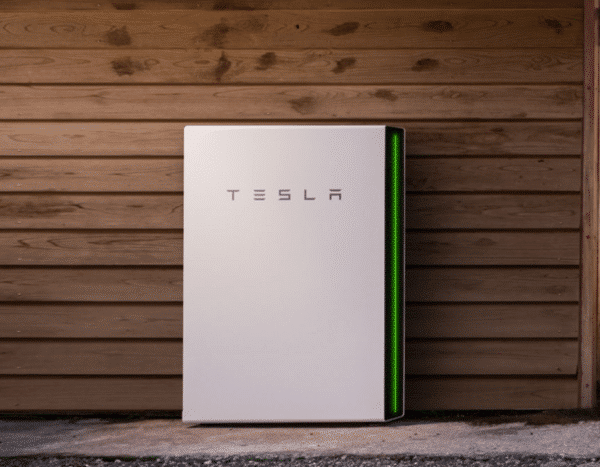 A tesla powerwall battery installed against a wooden wall.