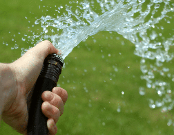 A hand holding a hose with water spraying out.