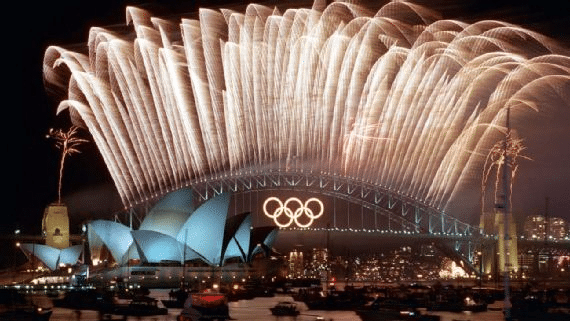 Fireworks display over sydney opera house with olympic rings illuminated on the harbour bridge.
