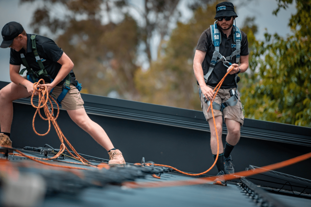 Two men working on a roof with ropes.