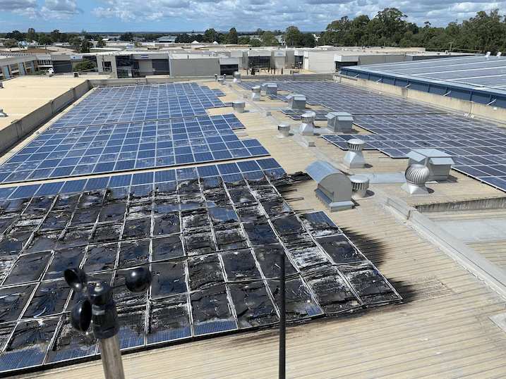 An array of solar panels on a rooftop with some showing signs of wear and visible dirt accumulations, surrounded by various roof vents and air ducts.